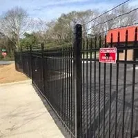 A black metal fence with a red sign on it is next to a parking lot.