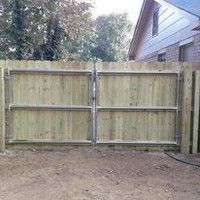 A wooden fence with a metal gate in front of a house.