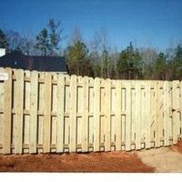 A wooden fence is sitting in the dirt in front of a house.