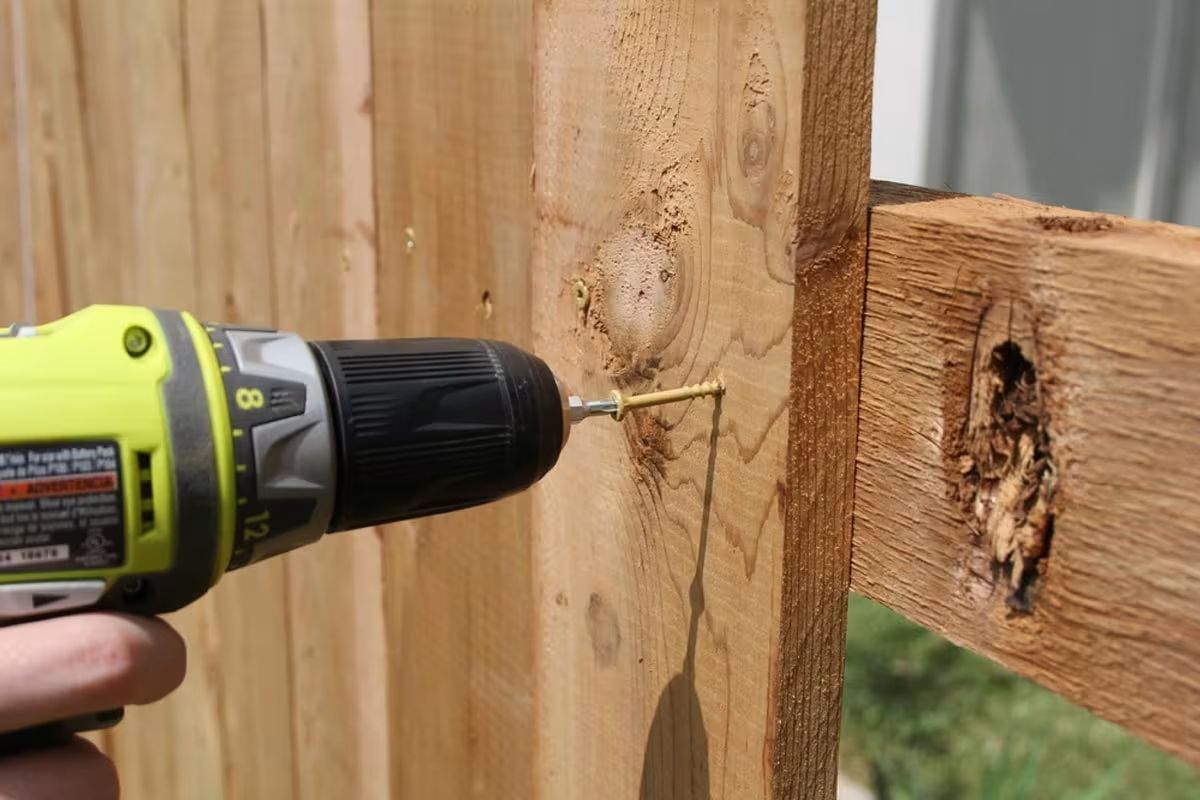 A person is using a drill to drill a hole in a wooden fence post.