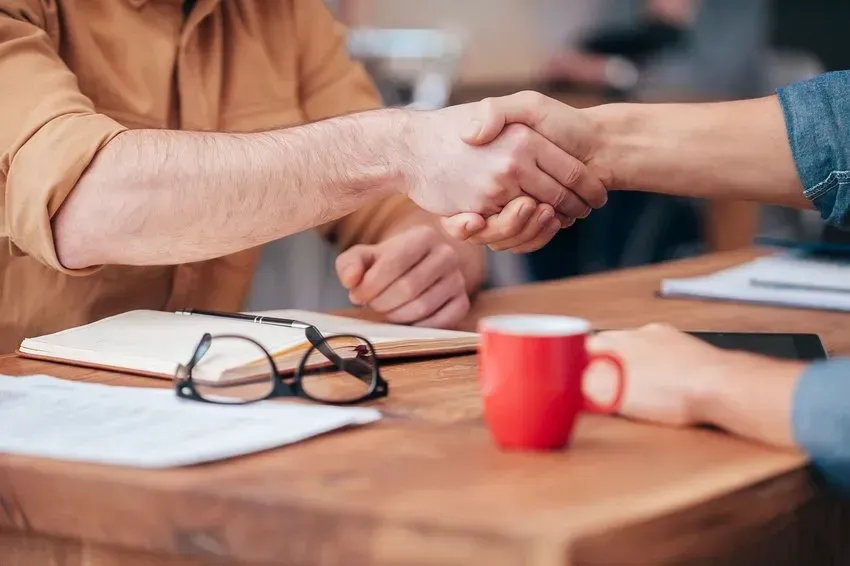 A man and a woman are shaking hands over a wooden table.