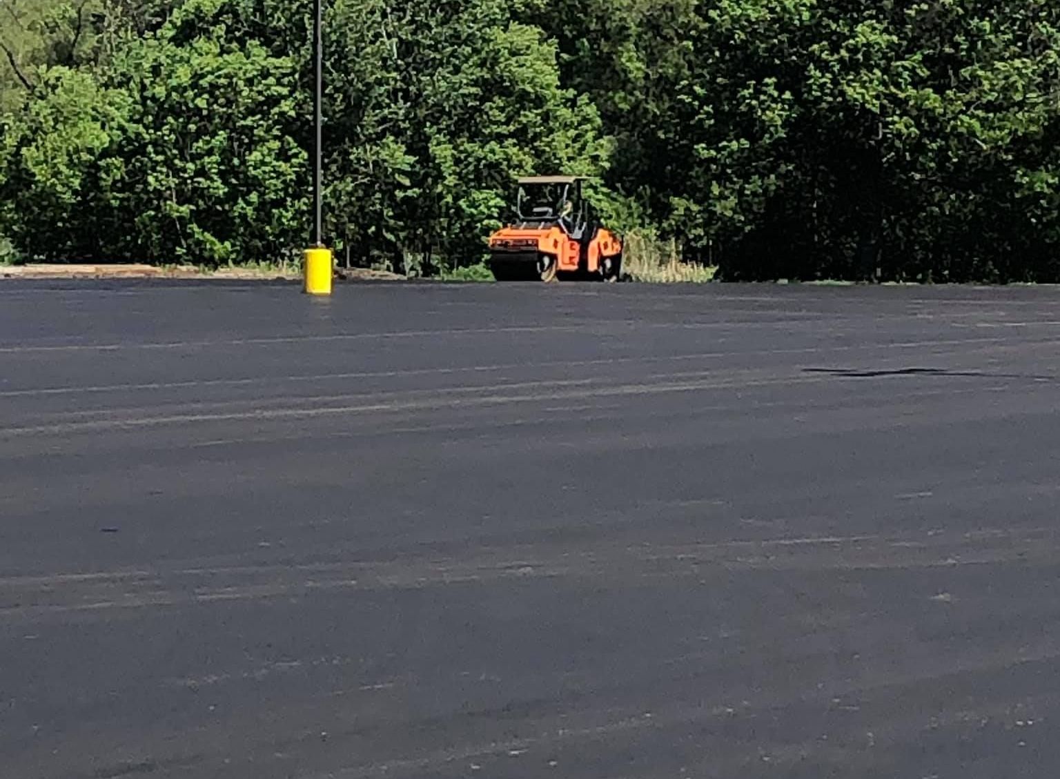 A roller is rolling asphalt in a parking lot.