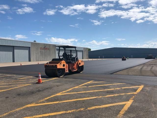 A roller is rolling asphalt in a parking lot.