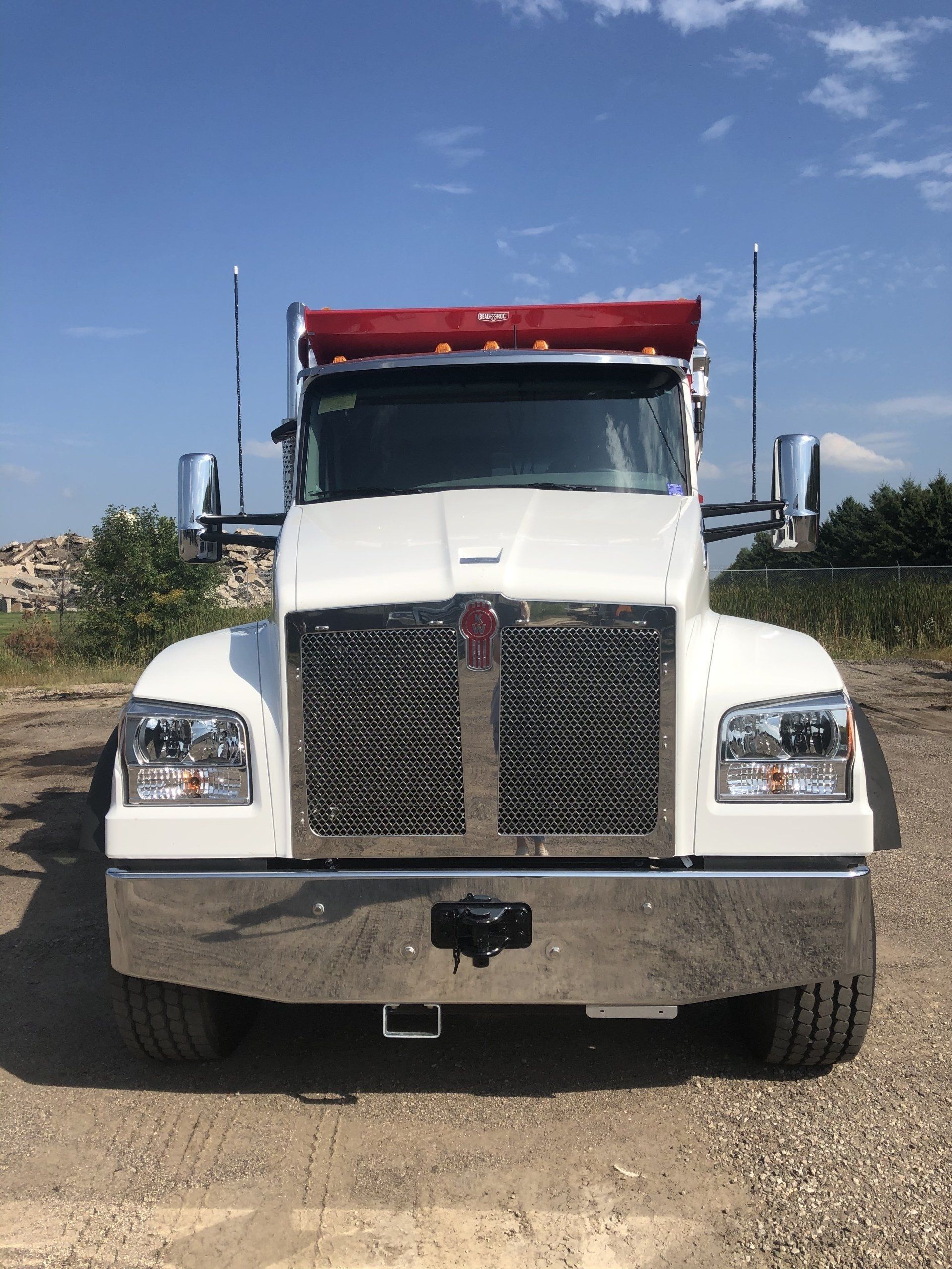 A white dump truck with a red roof is parked in a gravel lot.