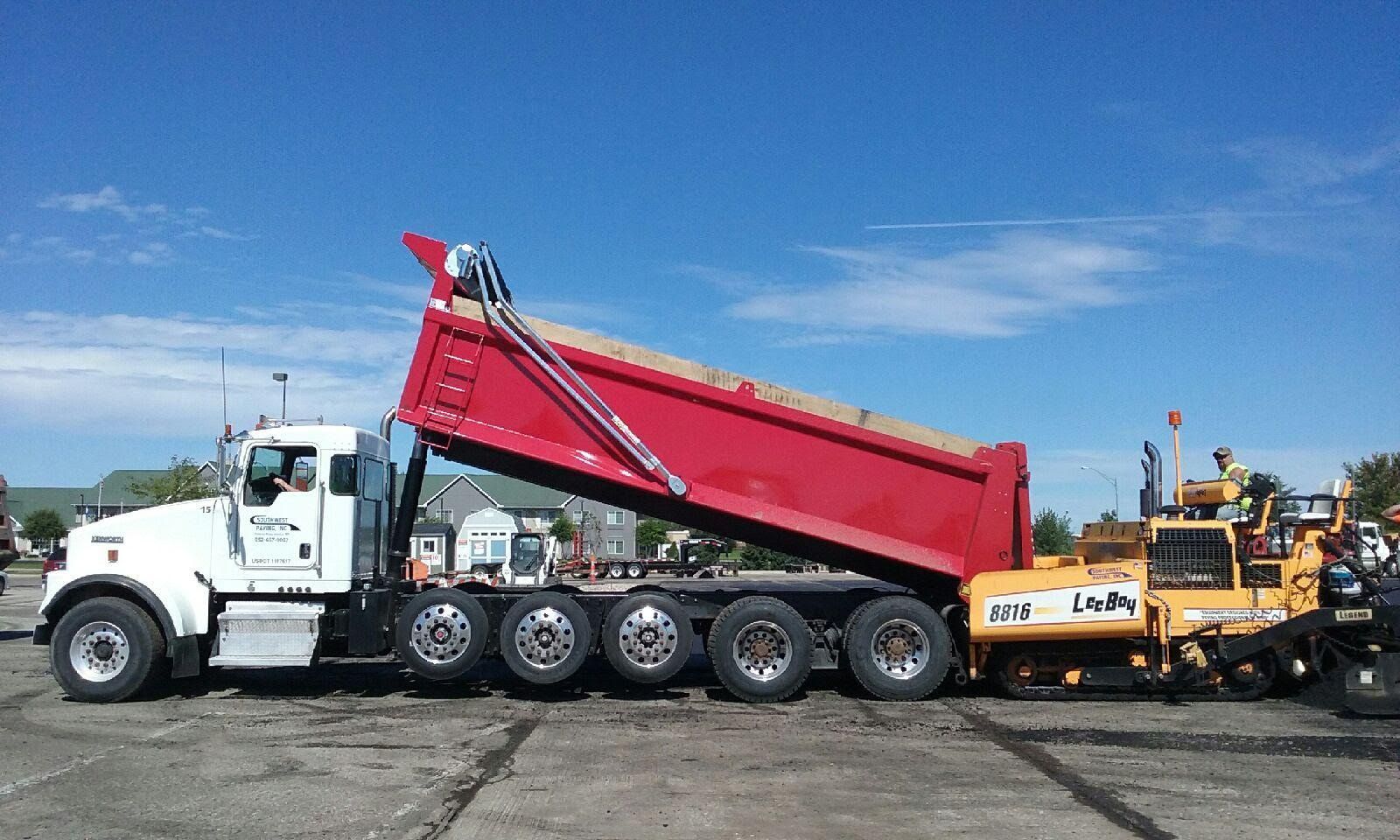A dump truck is parked in a parking lot next to a bulldozer.