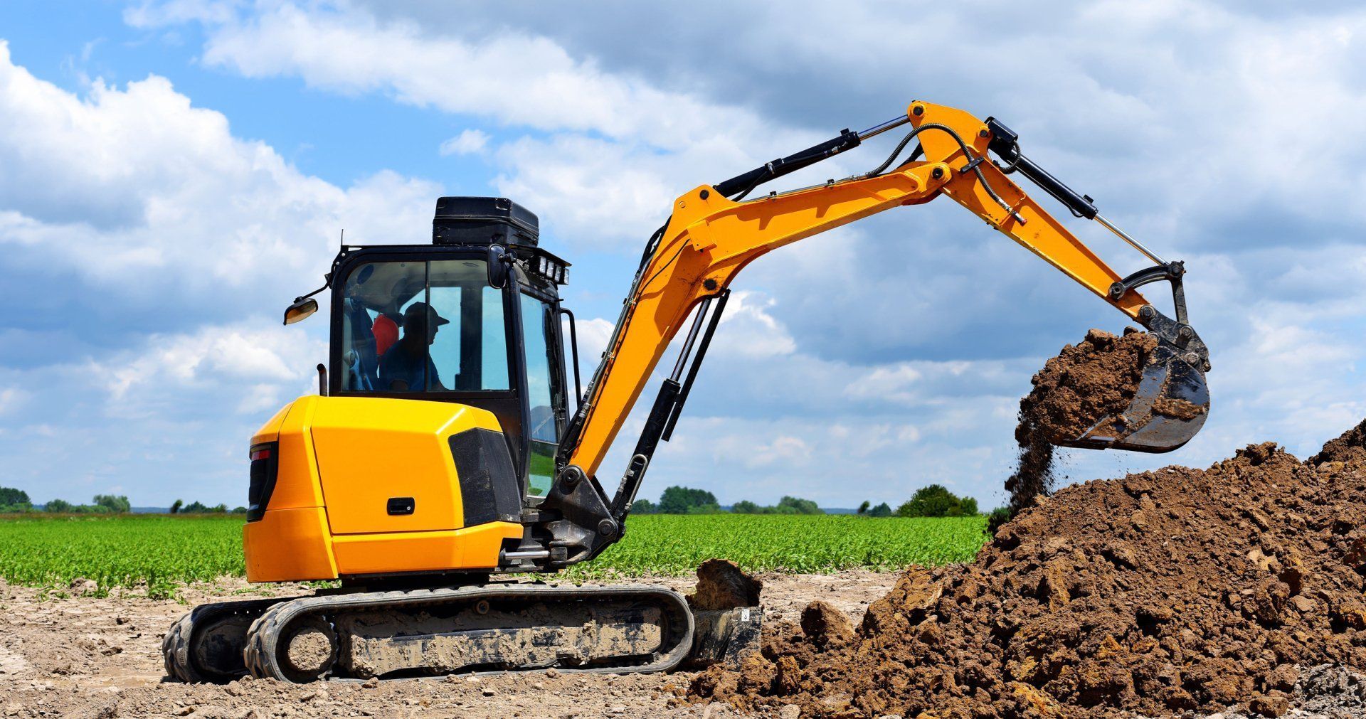 A yellow excavator is digging a hole in the dirt in a field.