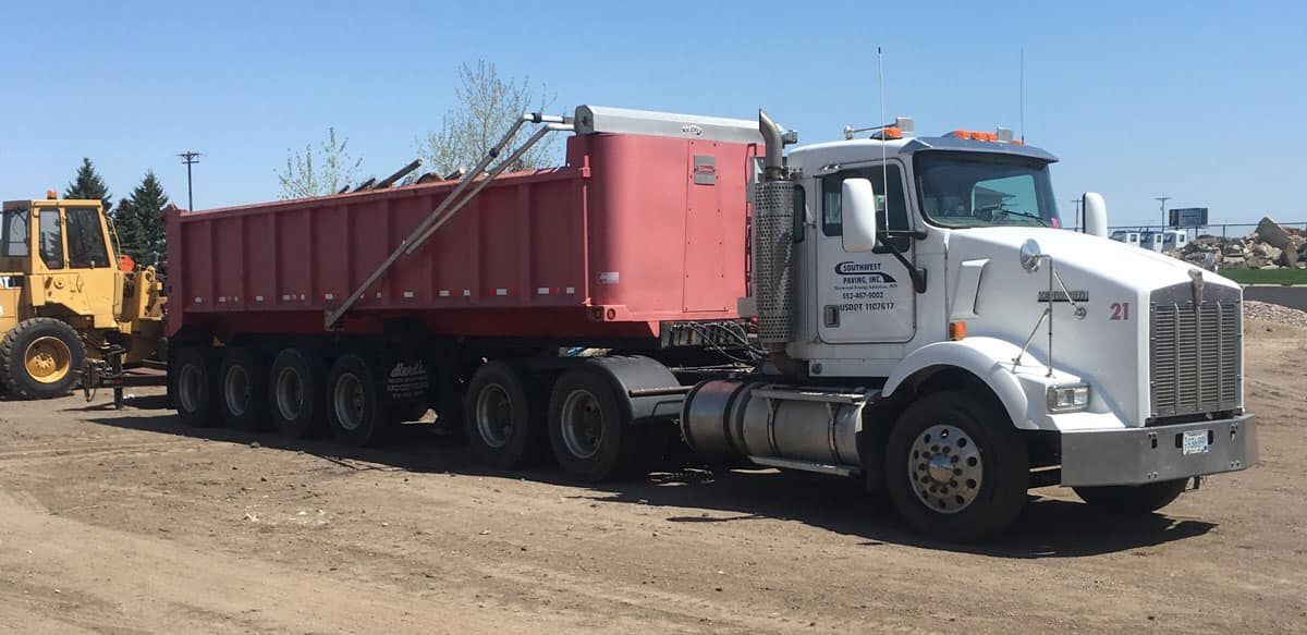 A dump truck is parked in a dirt lot next to a yellow tractor.