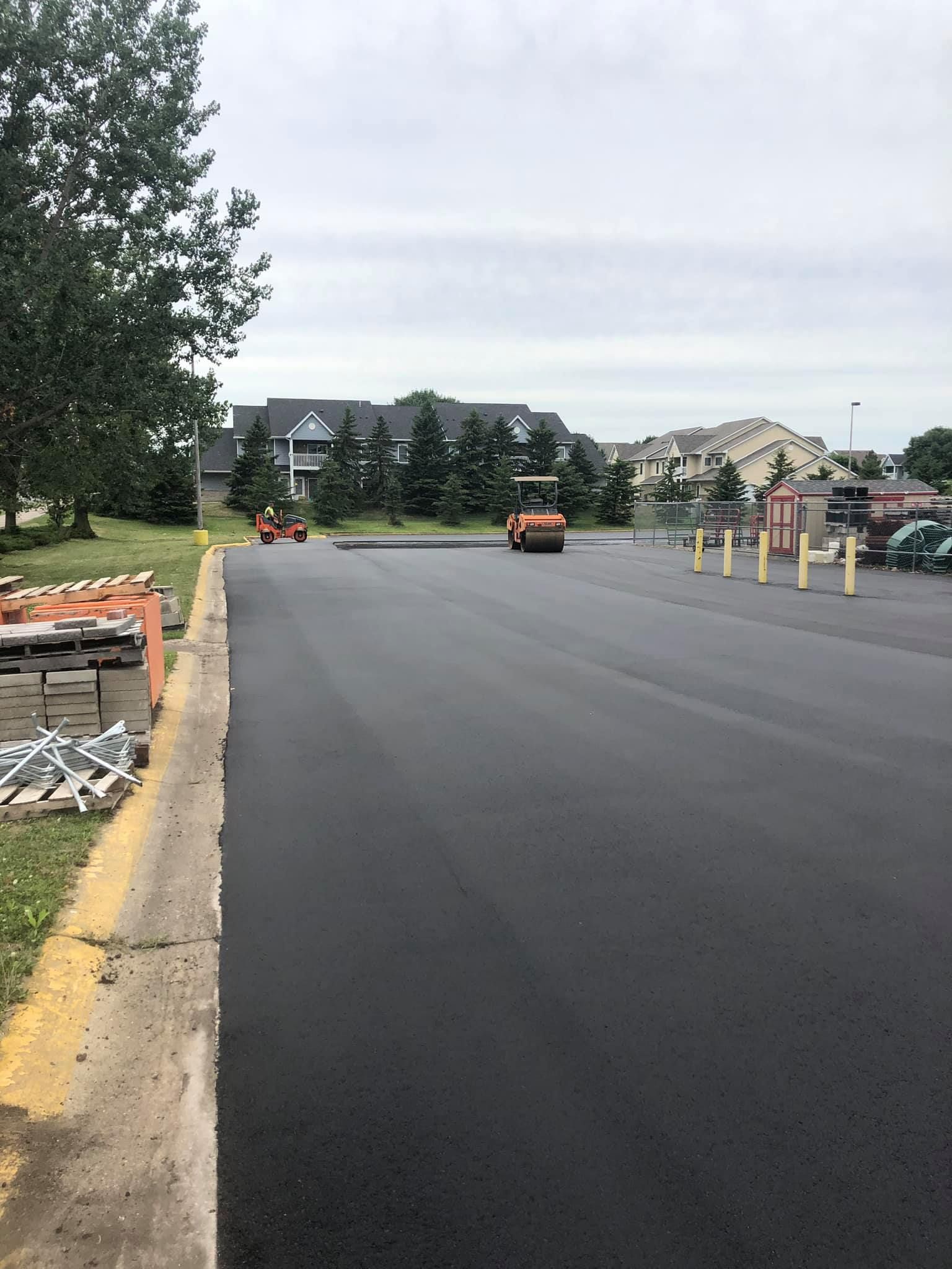A tractor is driving down a road next to a parking lot.