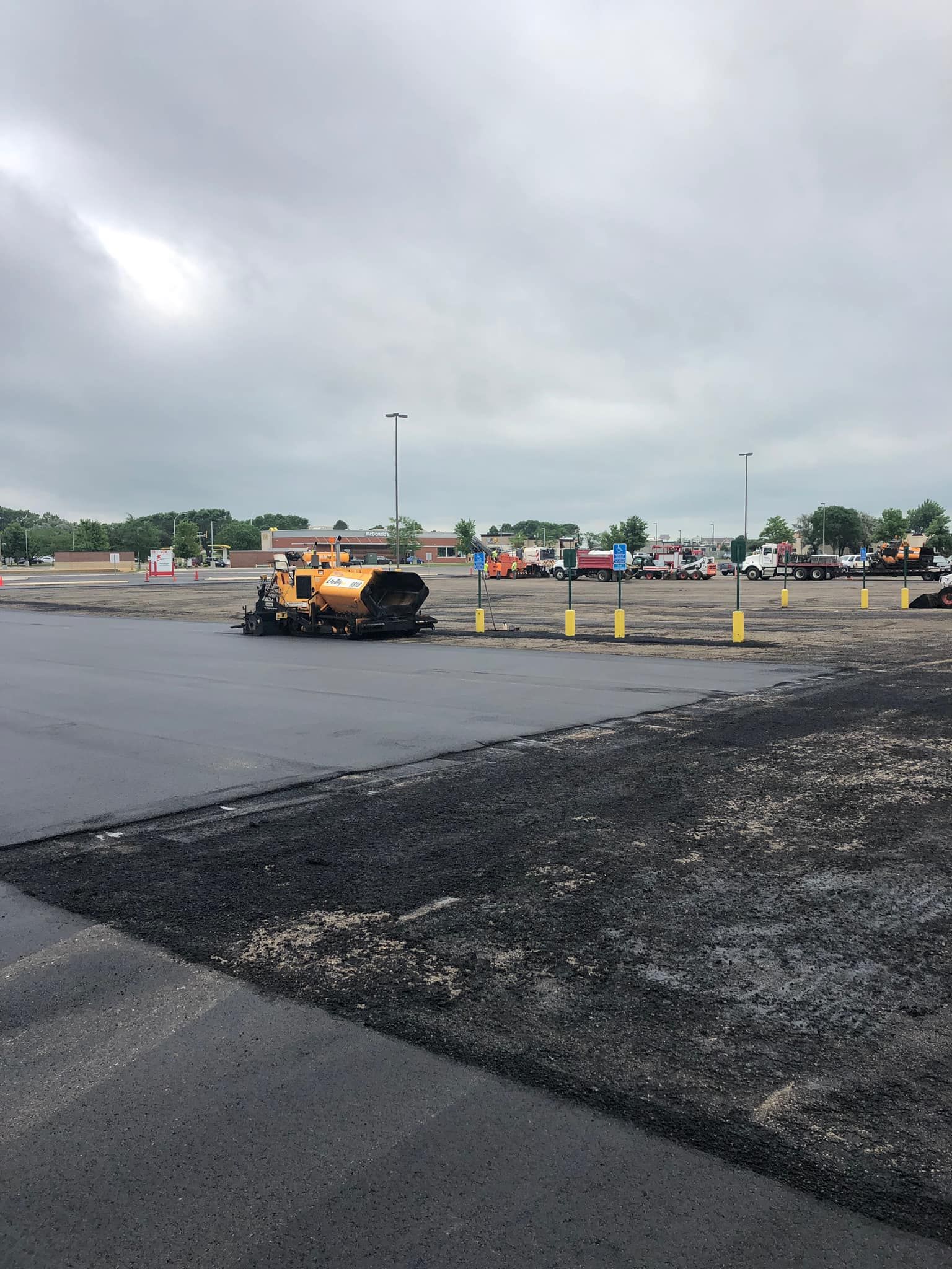 A yellow truck is paving a parking lot on a cloudy day.