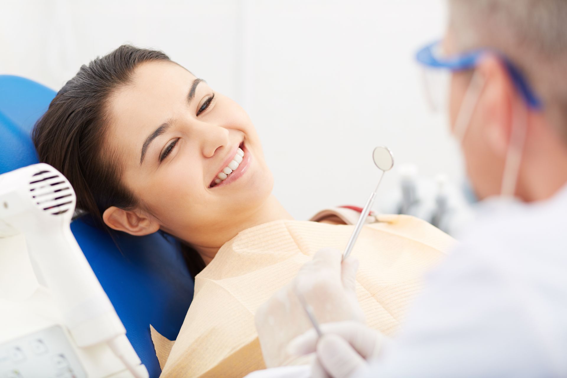 Woman smiling at dentist during a dental check-up; blue chair, bright setting.