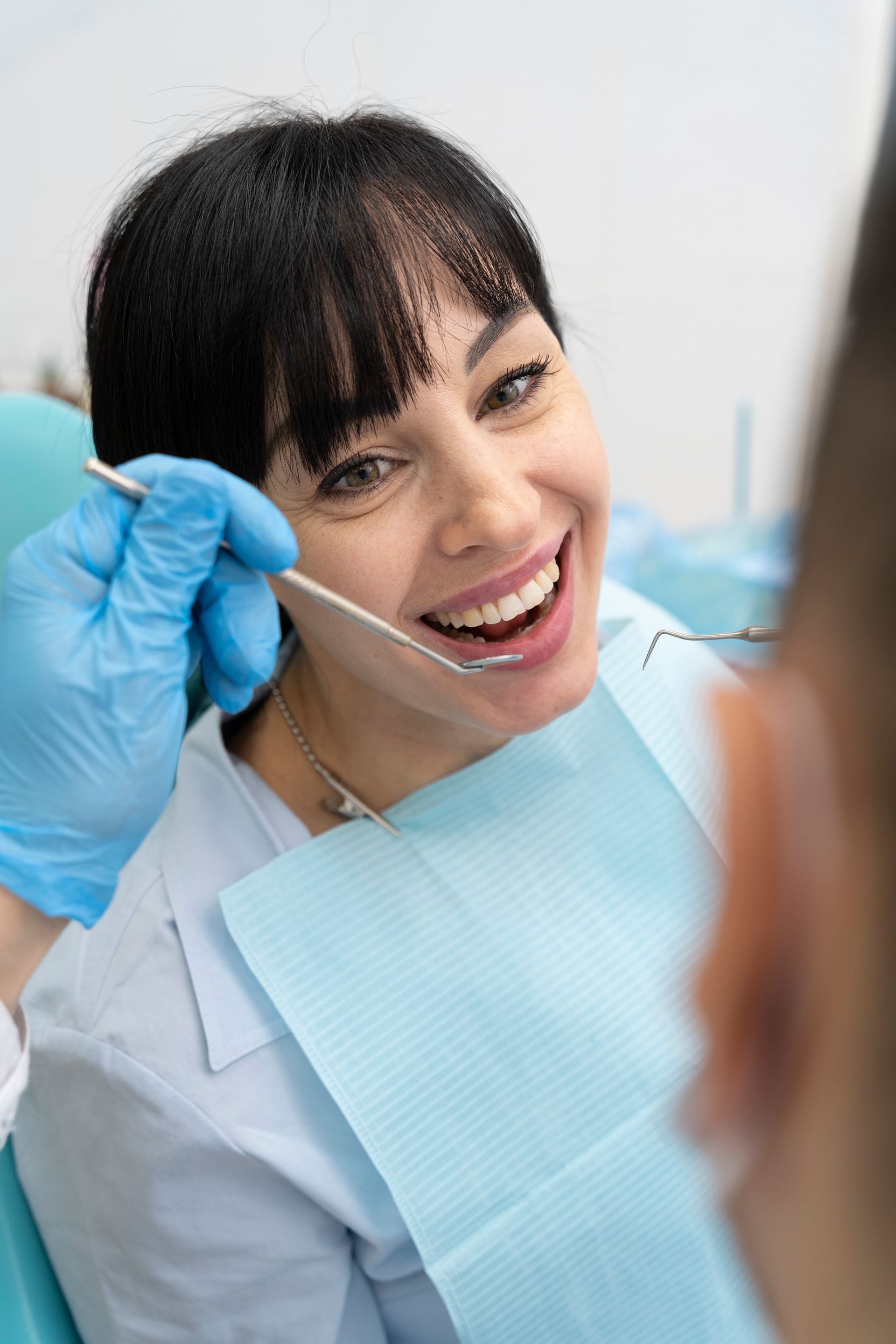 Woman at dentist, smiling, mouth open, being examined with a dental mirror in a dental office.