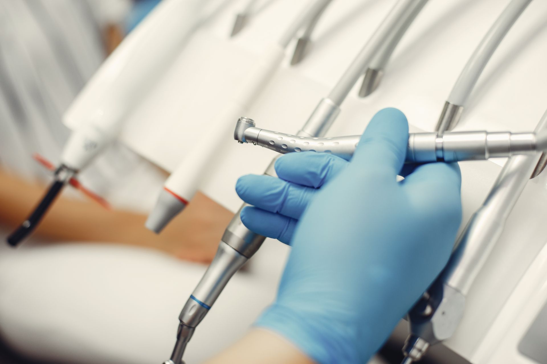 Dentist's gloved hand selects a dental tool from a rack of equipment in a white medical setting.