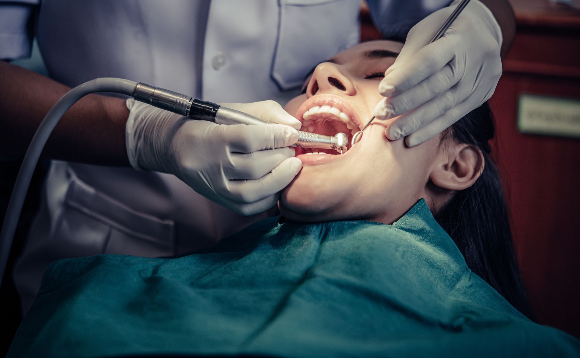 Dentist examining a patient's teeth with tools in a dental chair.