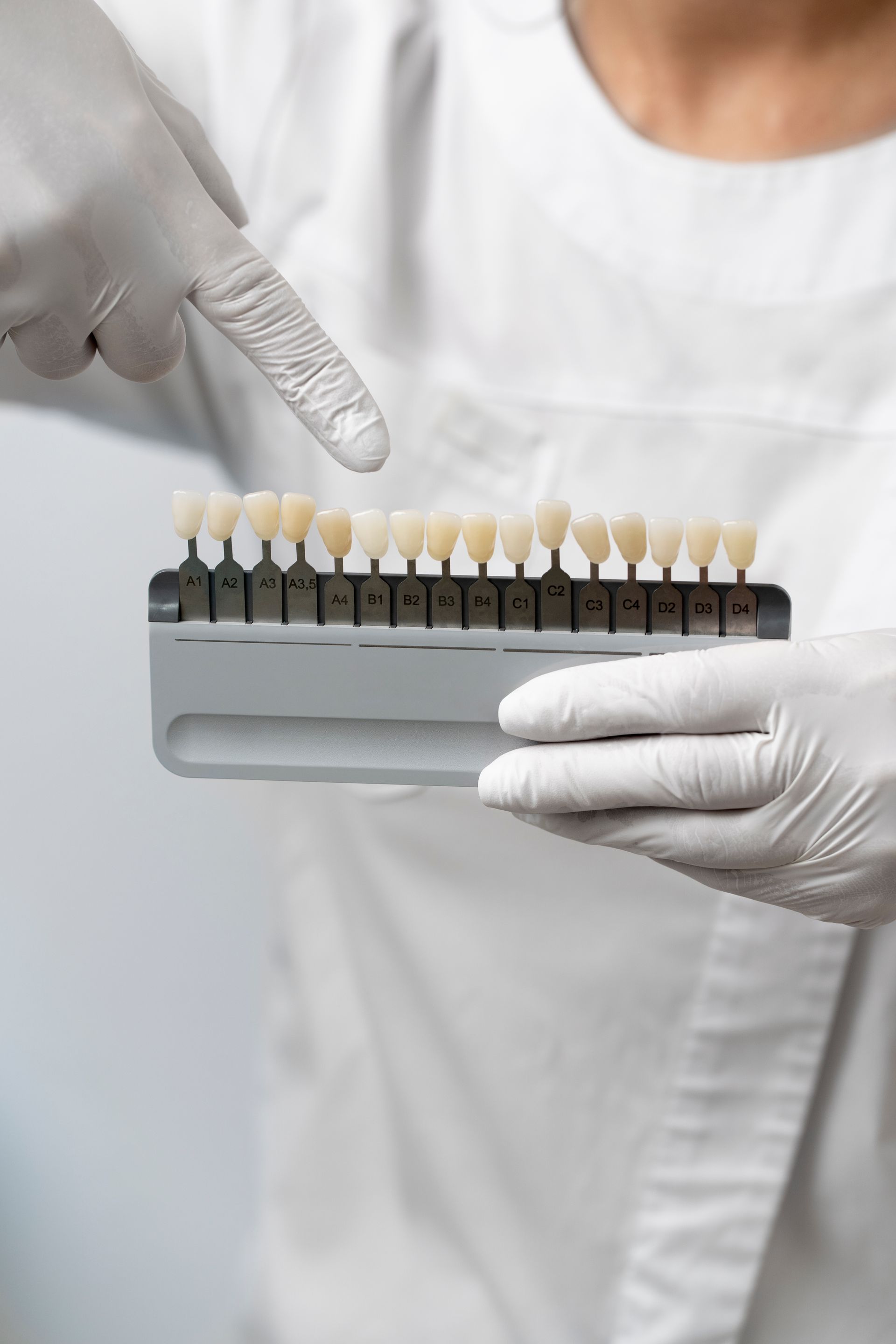 Dentist holding a shade guide, pointing to a tooth sample, comparing tooth color for a procedure.