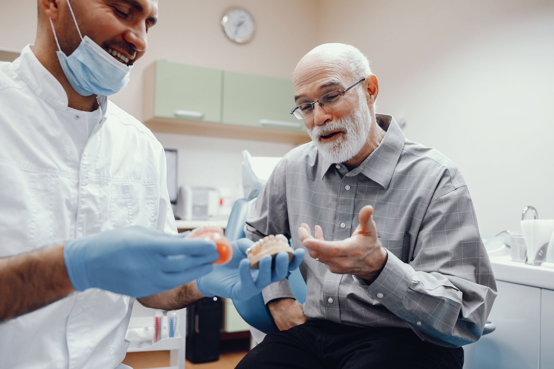 Dentist showing dentures to an older patient; both are smiling in a dental office.