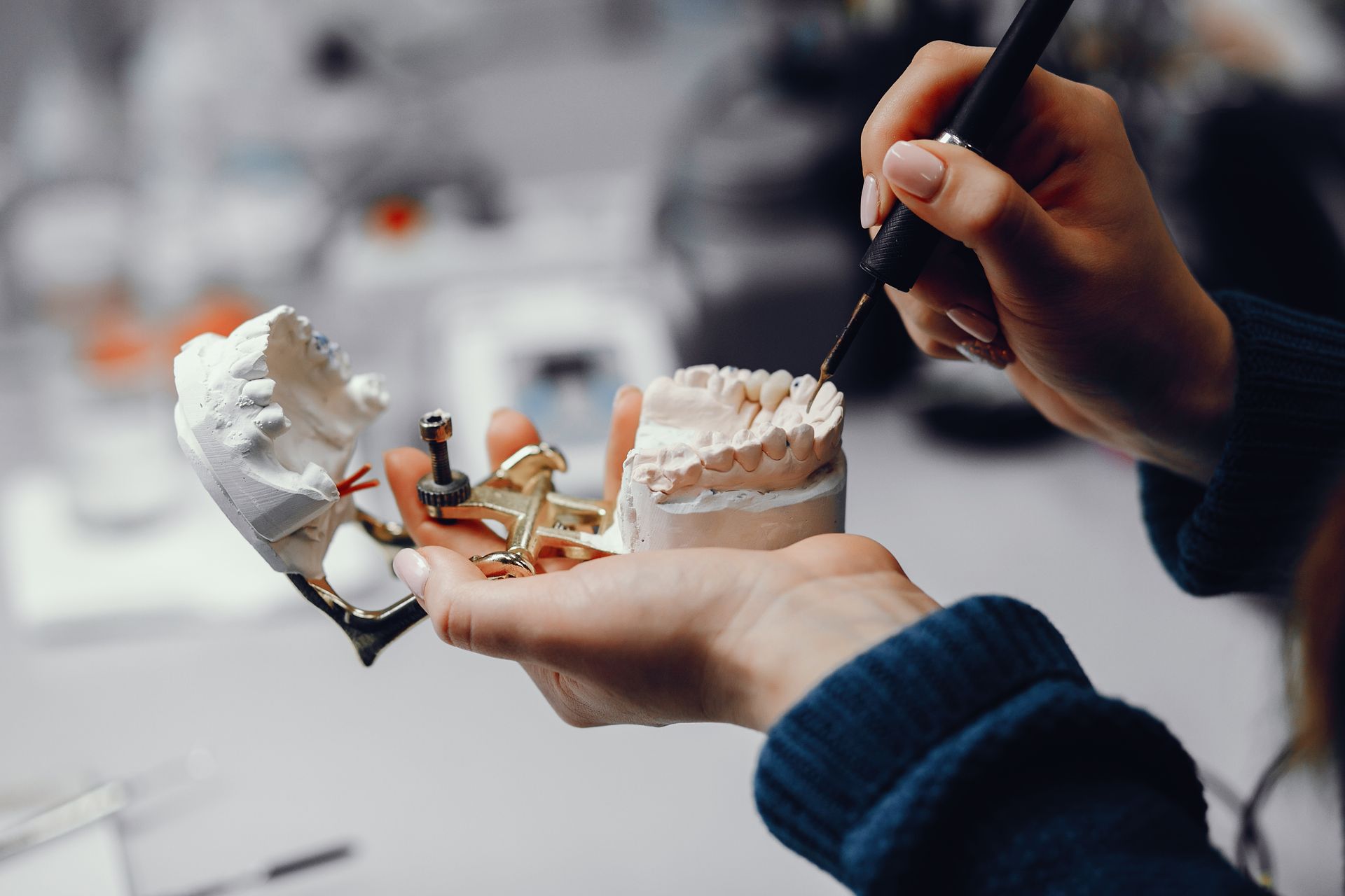 Hands shaping a dental mold with a tool in a lab setting.