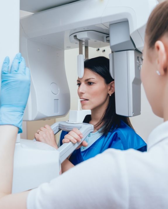 Dentist working on a patient in a dental office. Both wear masks. Bright light illuminates.