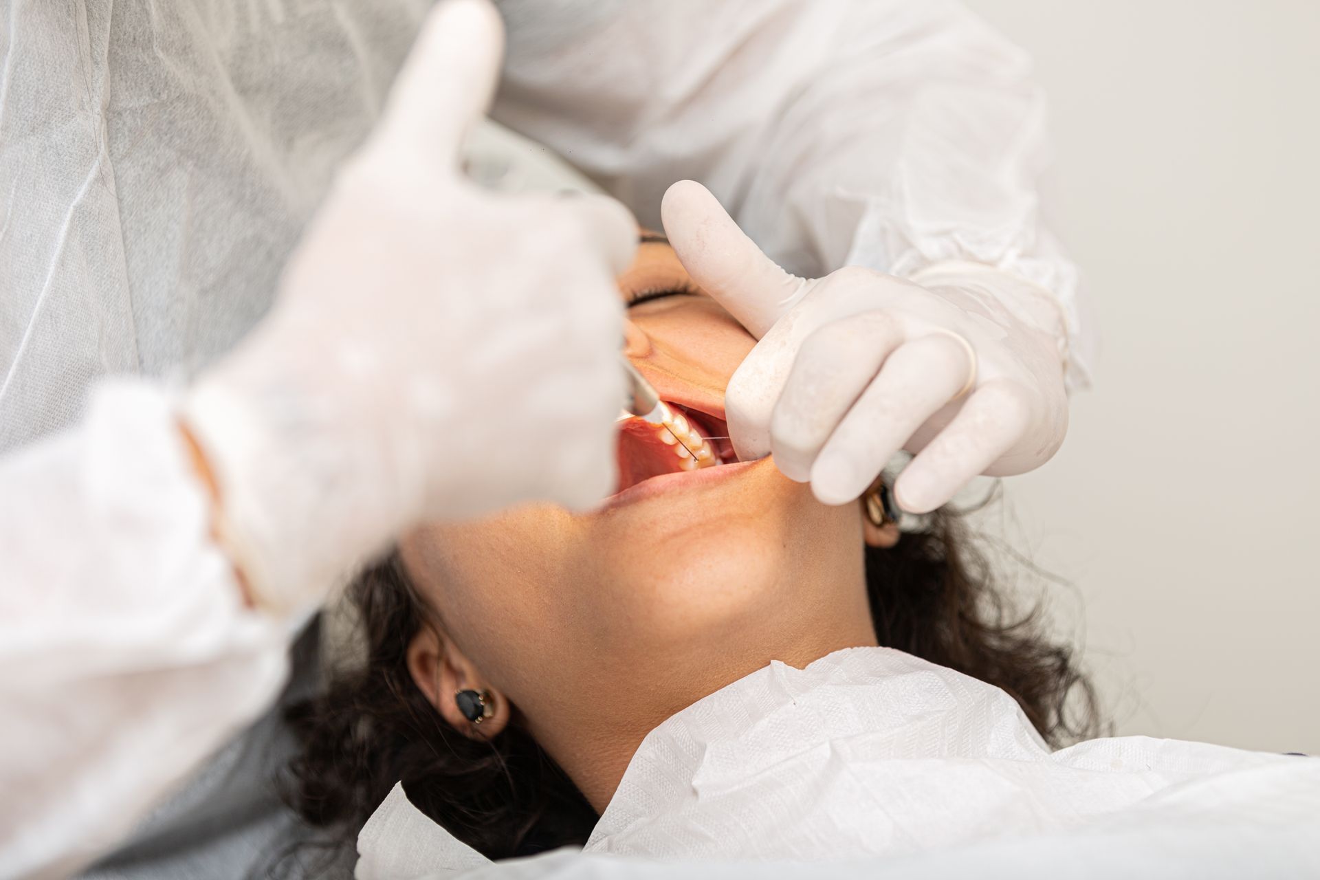 Dentist examining patient's mouth; both wear protective gear.