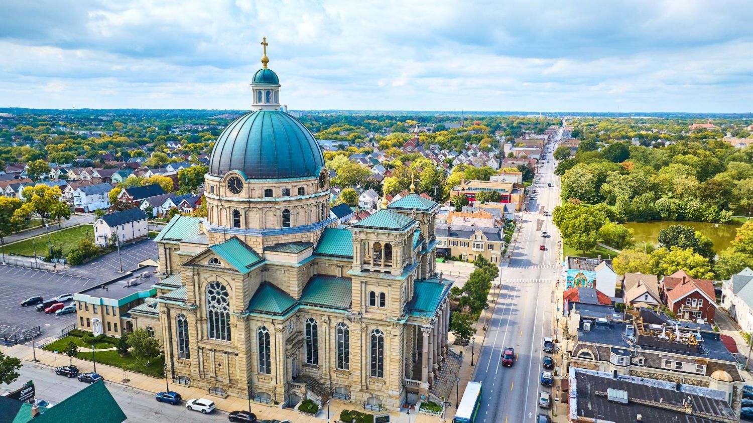 Aerial view of a large church with a teal dome, overlooking a city street with buildings and trees.