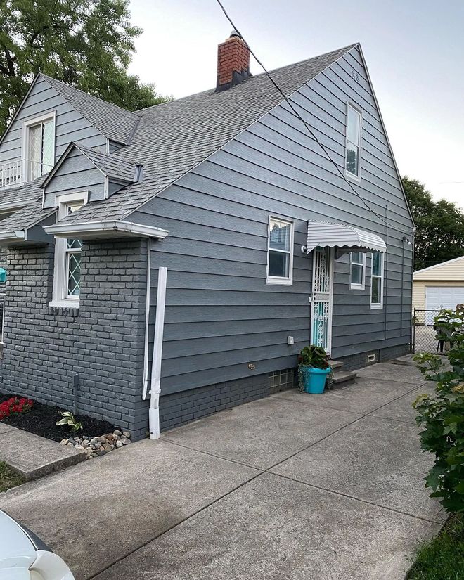 A gray house with a blue door and a blue potted plant in front of it.