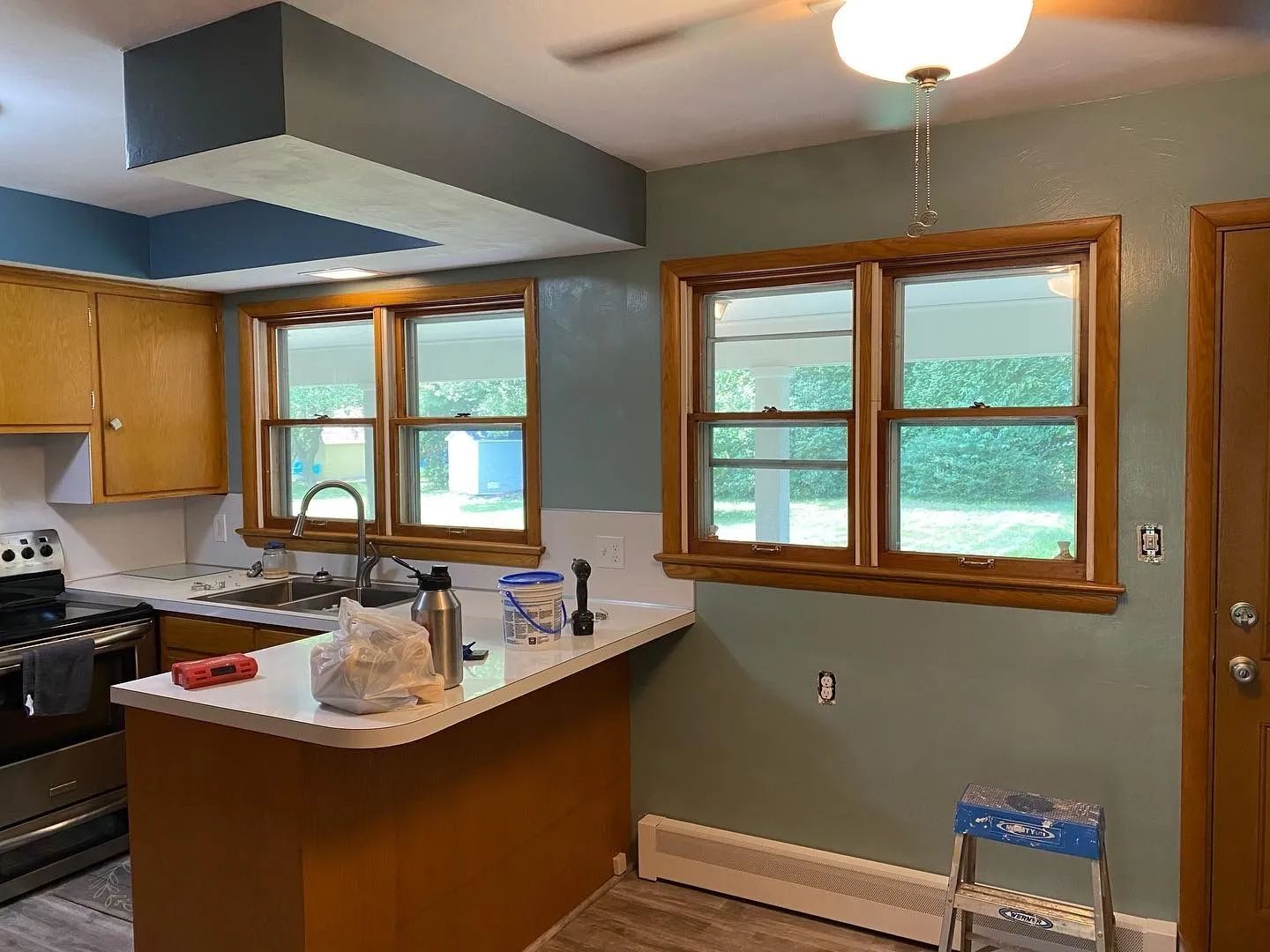 A kitchen with a stove , sink , and two windows.