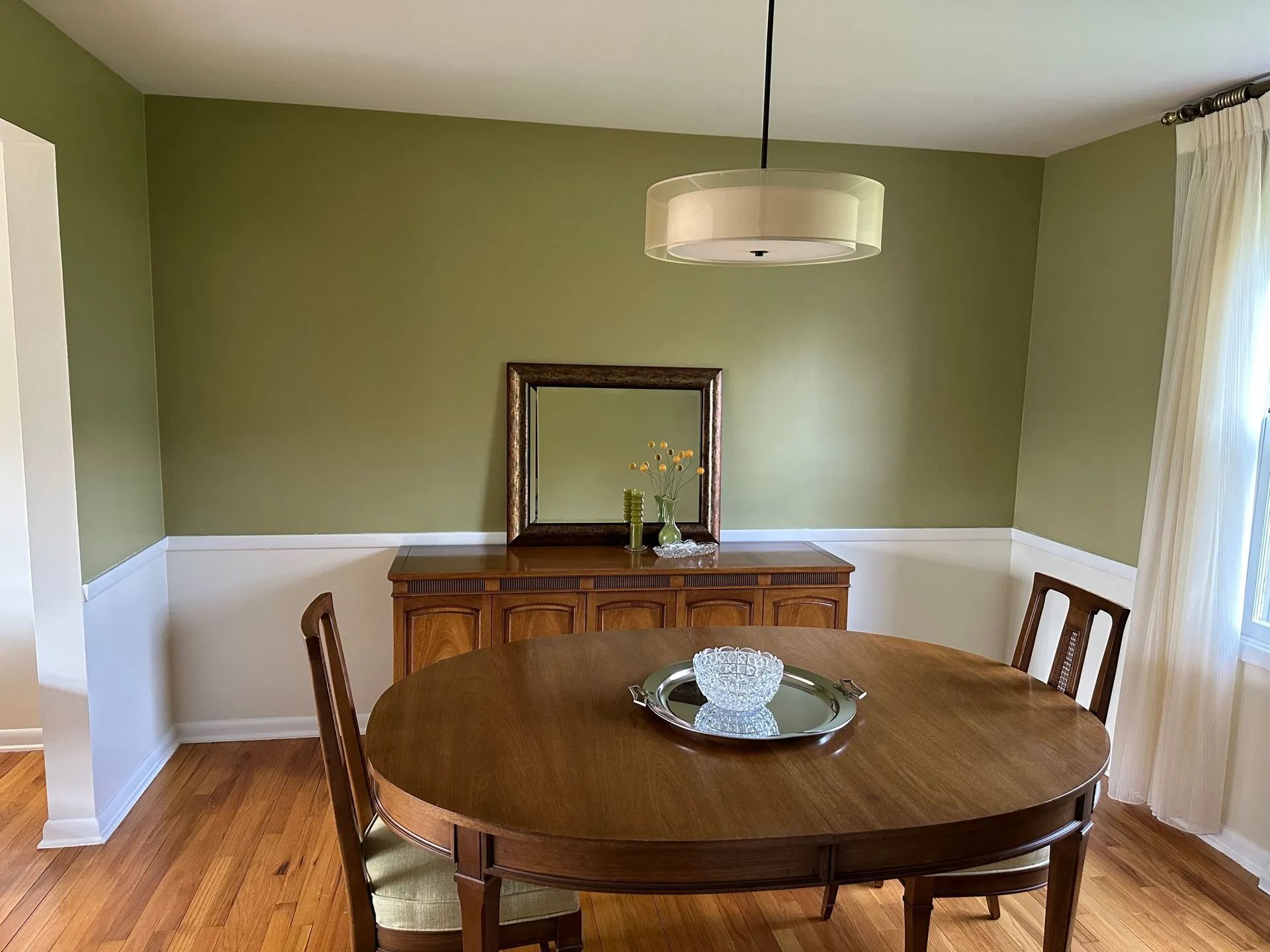 A dining room with a round table and chairs and a mirror.