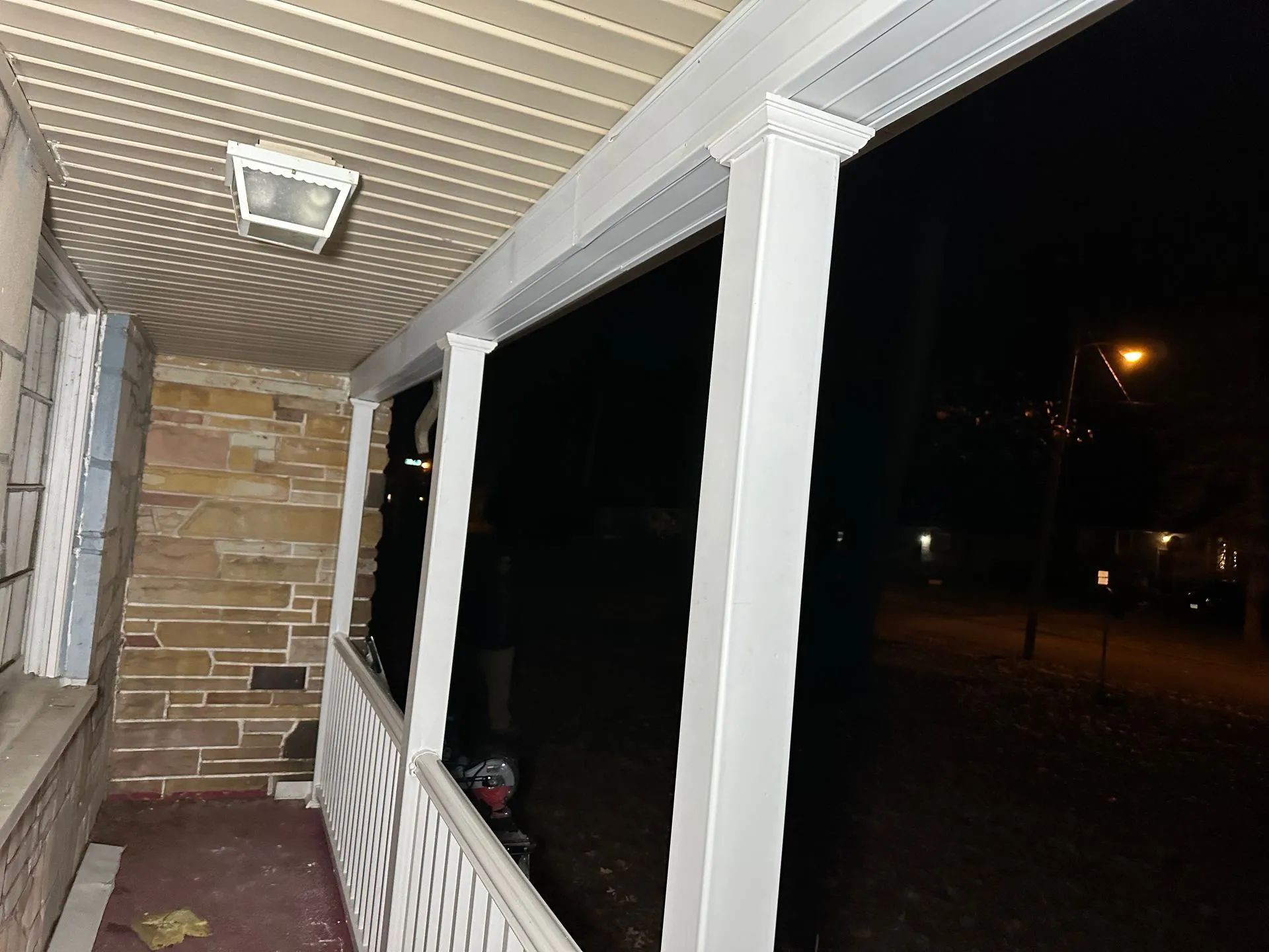 A porch with a brick wall and a white railing at night