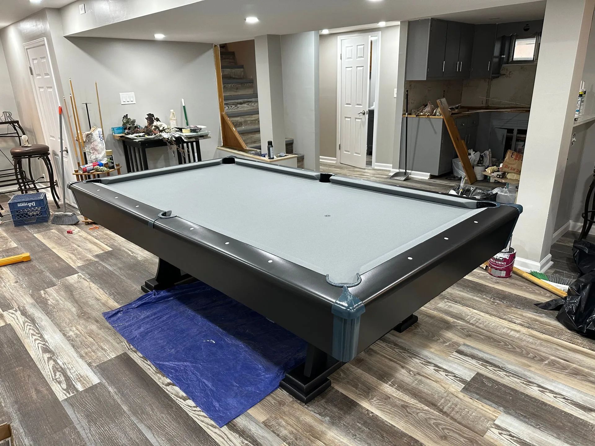 A pool table is sitting on a blue tarp in a basement.