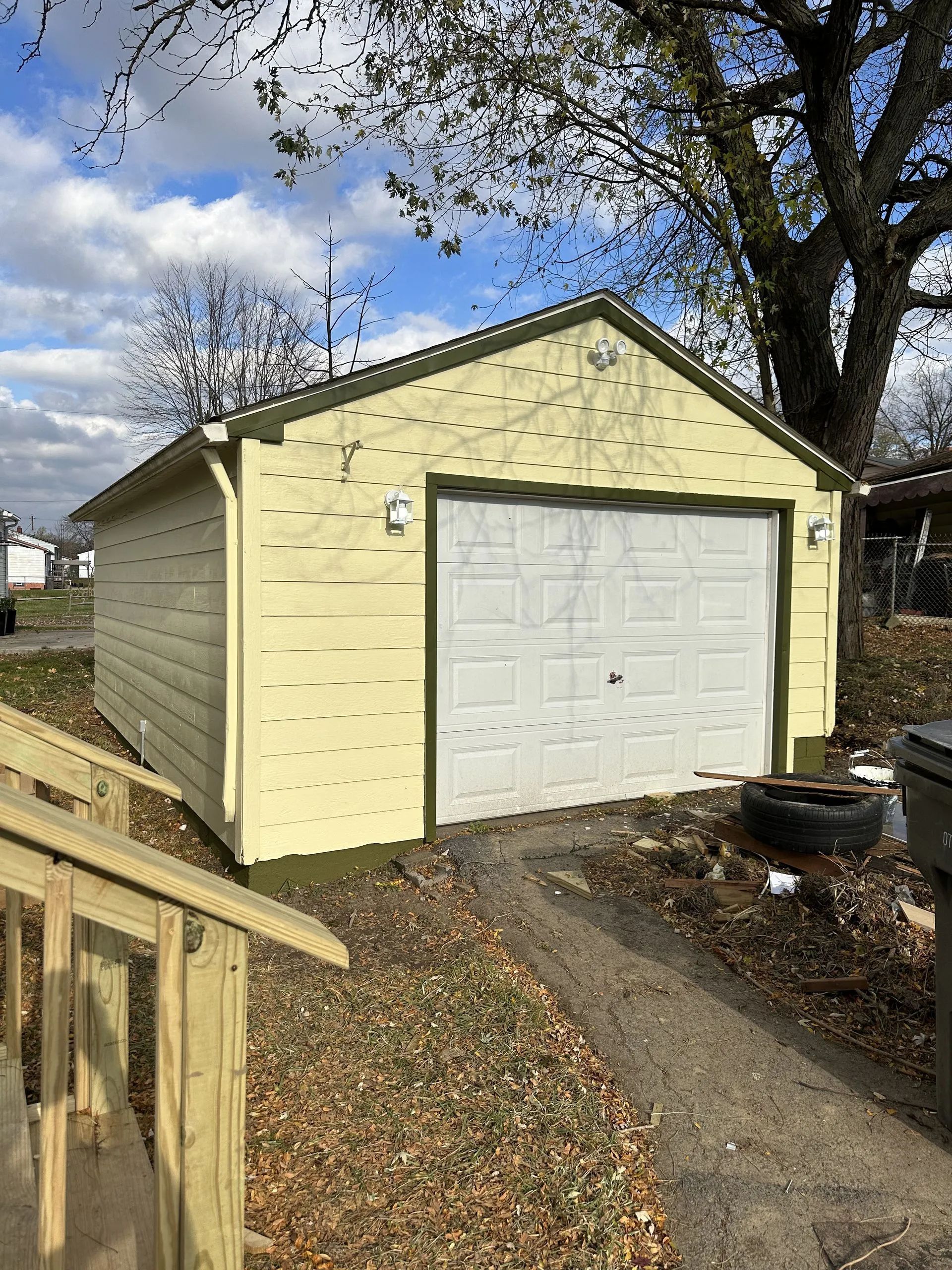 A yellow garage with a white door and a tree in the background.