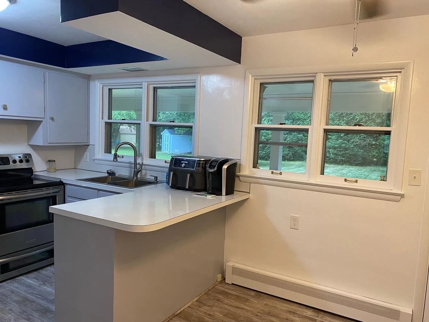 A kitchen with white cabinets , a sink , a stove , and two windows.