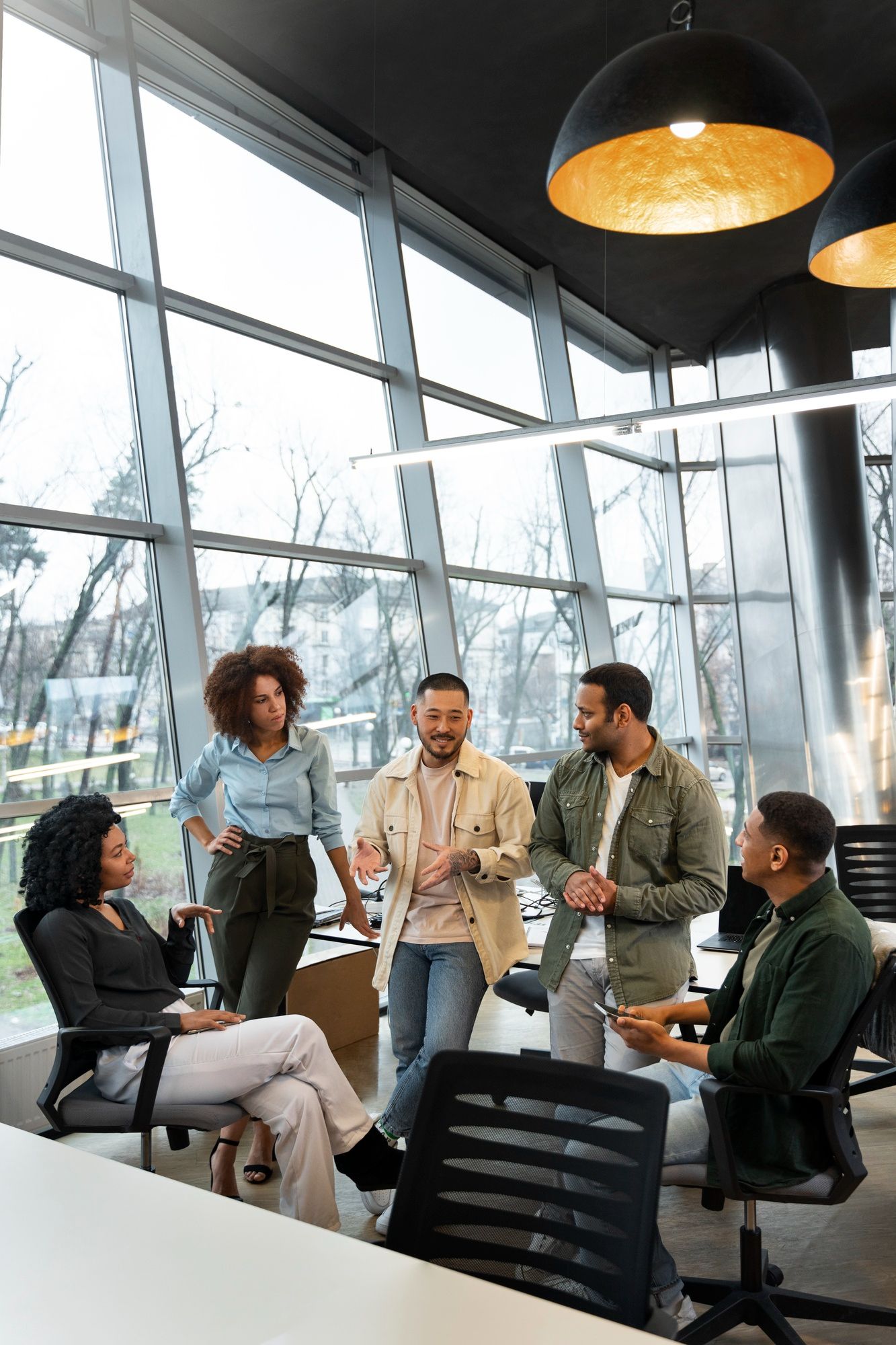 A diverse group of colleagues conversing in a modern office with large floor-to-ceiling windows.