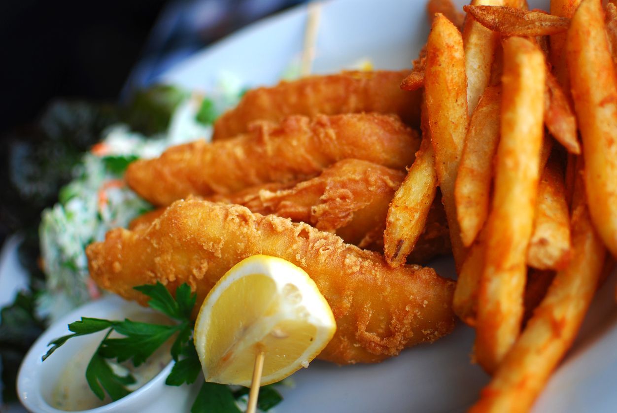 Fish and chips with lemon wedge and coleslaw on a white plate.