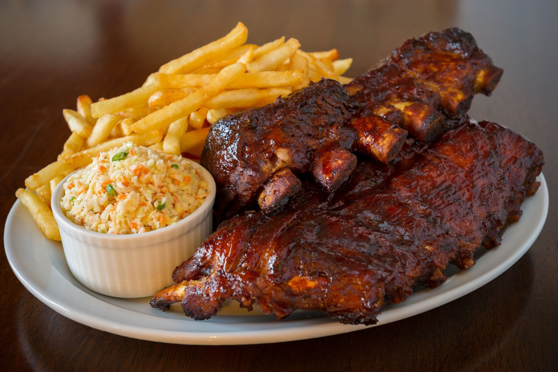Plate of ribs, french fries, and coleslaw. Ribs are glazed in dark sauce.