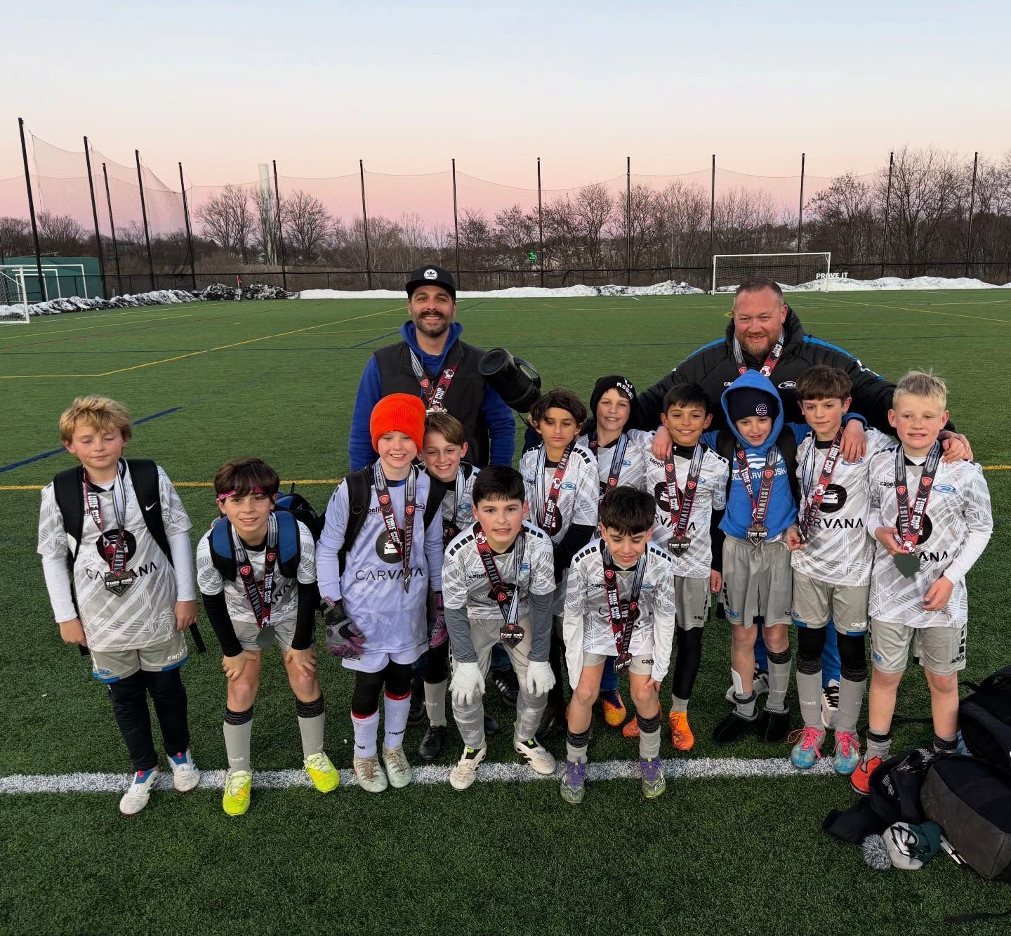 Youth soccer team and coaches on a field, all wearing medals.