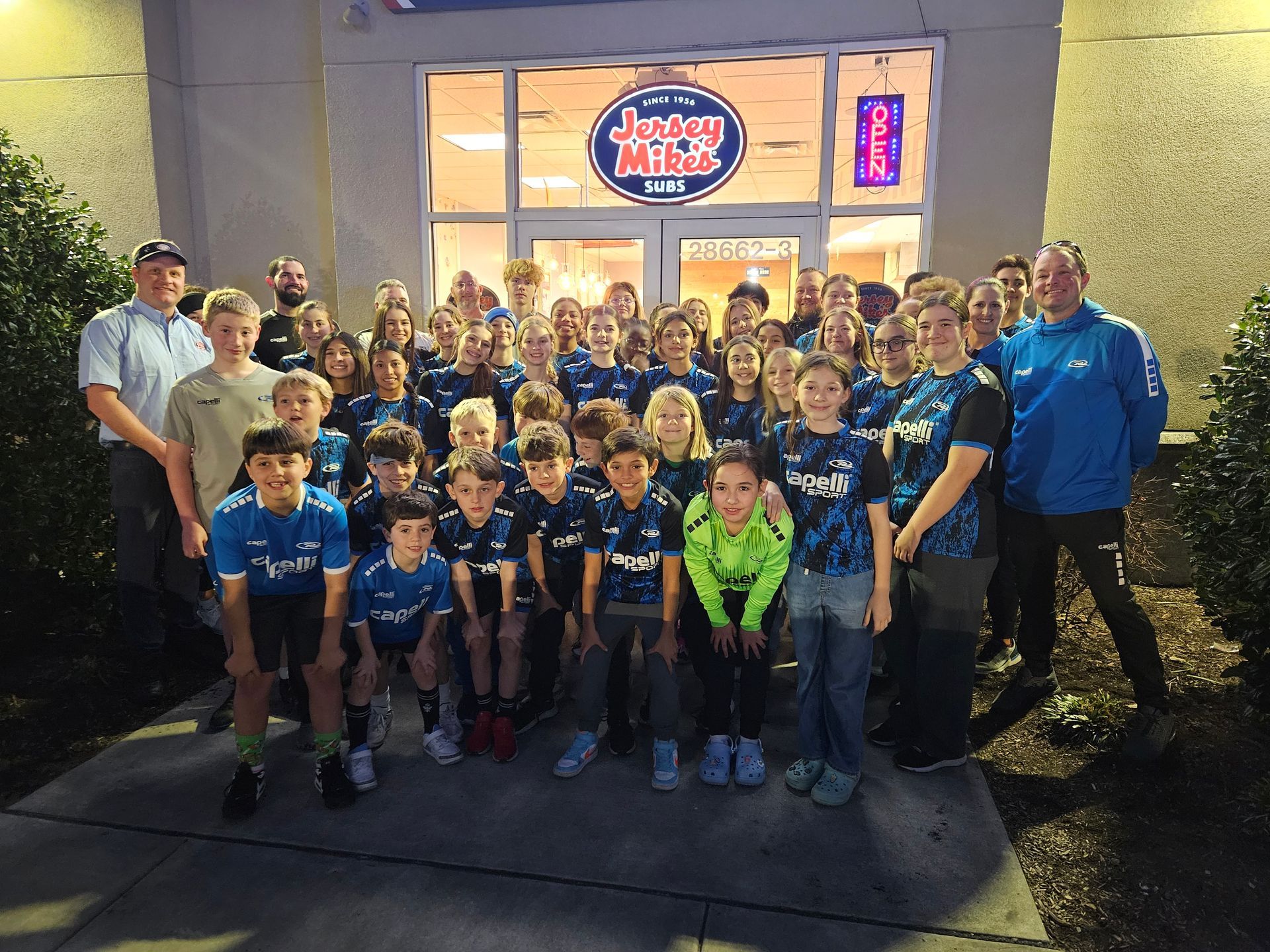 A group of people posing for a picture in front of a jersey mike's restaurant