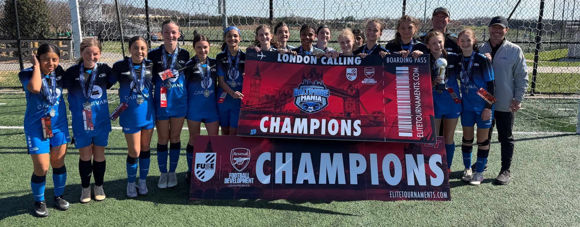 A soccer team in blue and black uniforms stands on a field holding two large 