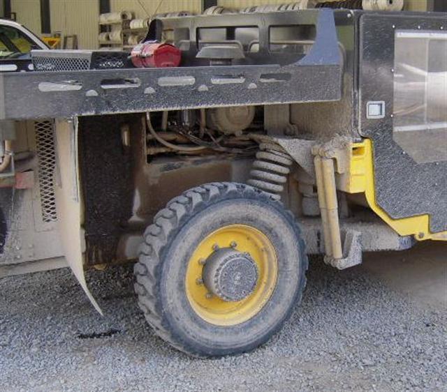 A front wheel of a yellow and black heavy-duty vehicle is visible on a gravel surface.