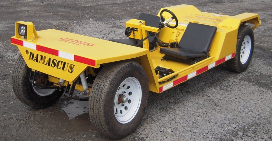 Yellow Damascus baggage tug vehicle with seats, white tires, and red/white stripes.