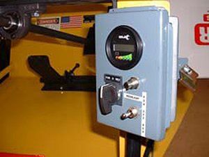 Gray control box with a digital display, key switch, and gauges mounted on a yellow machine.