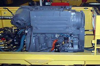 Gray diesel engine in a yellow machine frame, showing various hoses and components.
