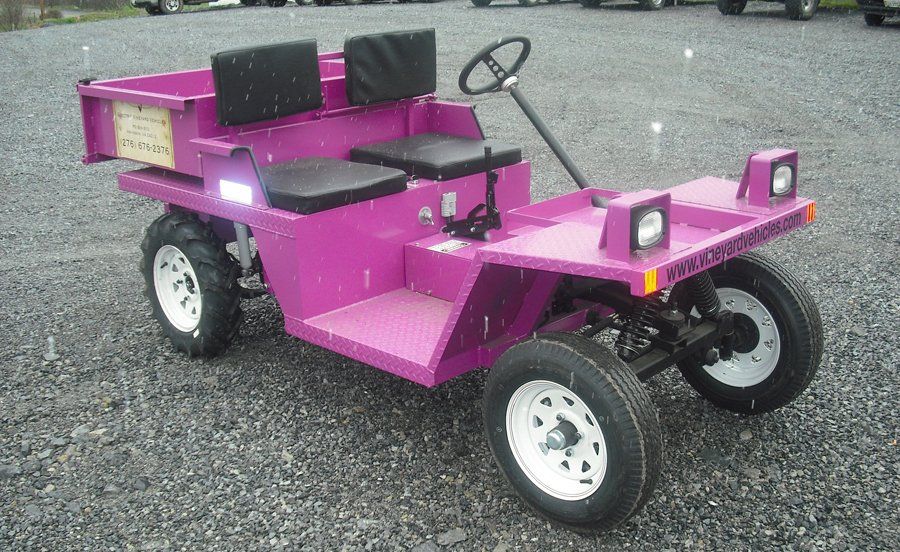 Pink utility vehicle with a dump bed, two seats, and a steering wheel, parked on gravel.
