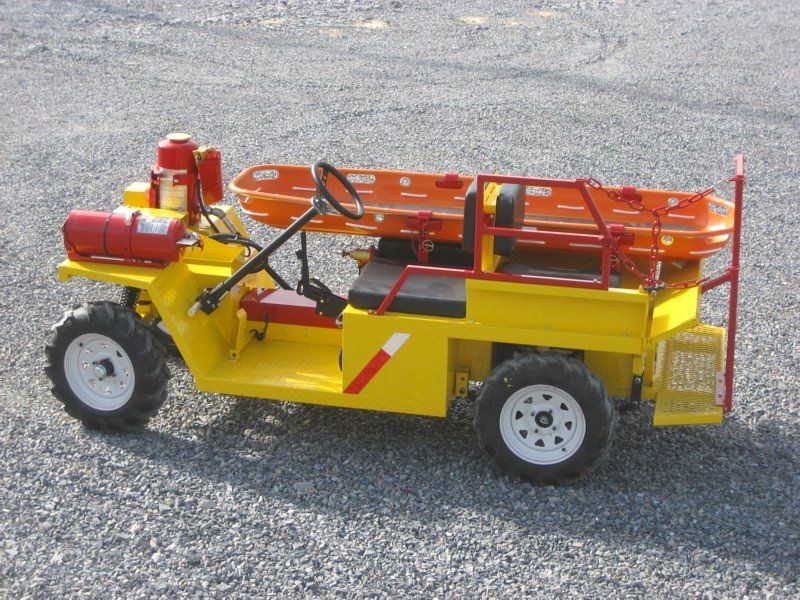 Yellow rescue vehicle with orange stretcher, on gravel.