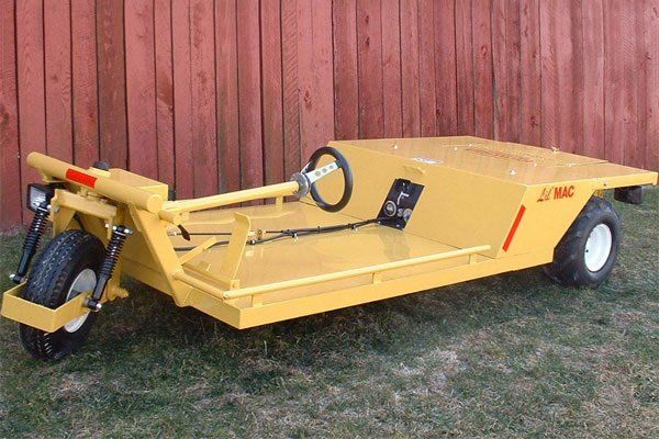 Yellow agricultural mower with a single front wheel, steering wheel, and open platform on a grassy area.