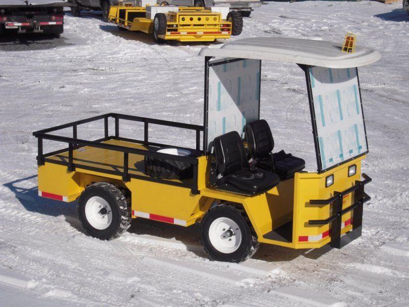Yellow utility vehicle on snowy ground, with two seats, a cargo bed, and a canopy.