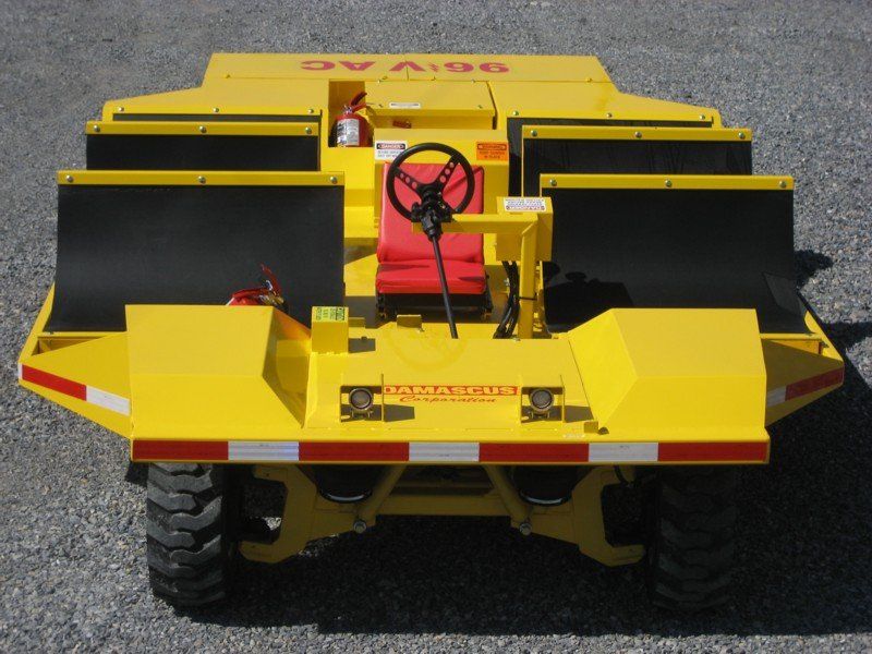 Yellow industrial vehicle with black panels and steering wheel, viewed from the rear on a gravel surface.