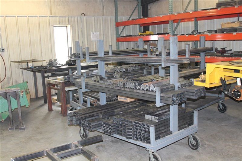 Metal stock in a warehouse on a rolling cart with shelving. Shelving and other metal on other racks.