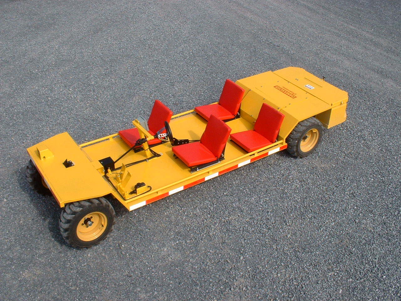 Yellow passenger transport vehicle with red seats on gravel.