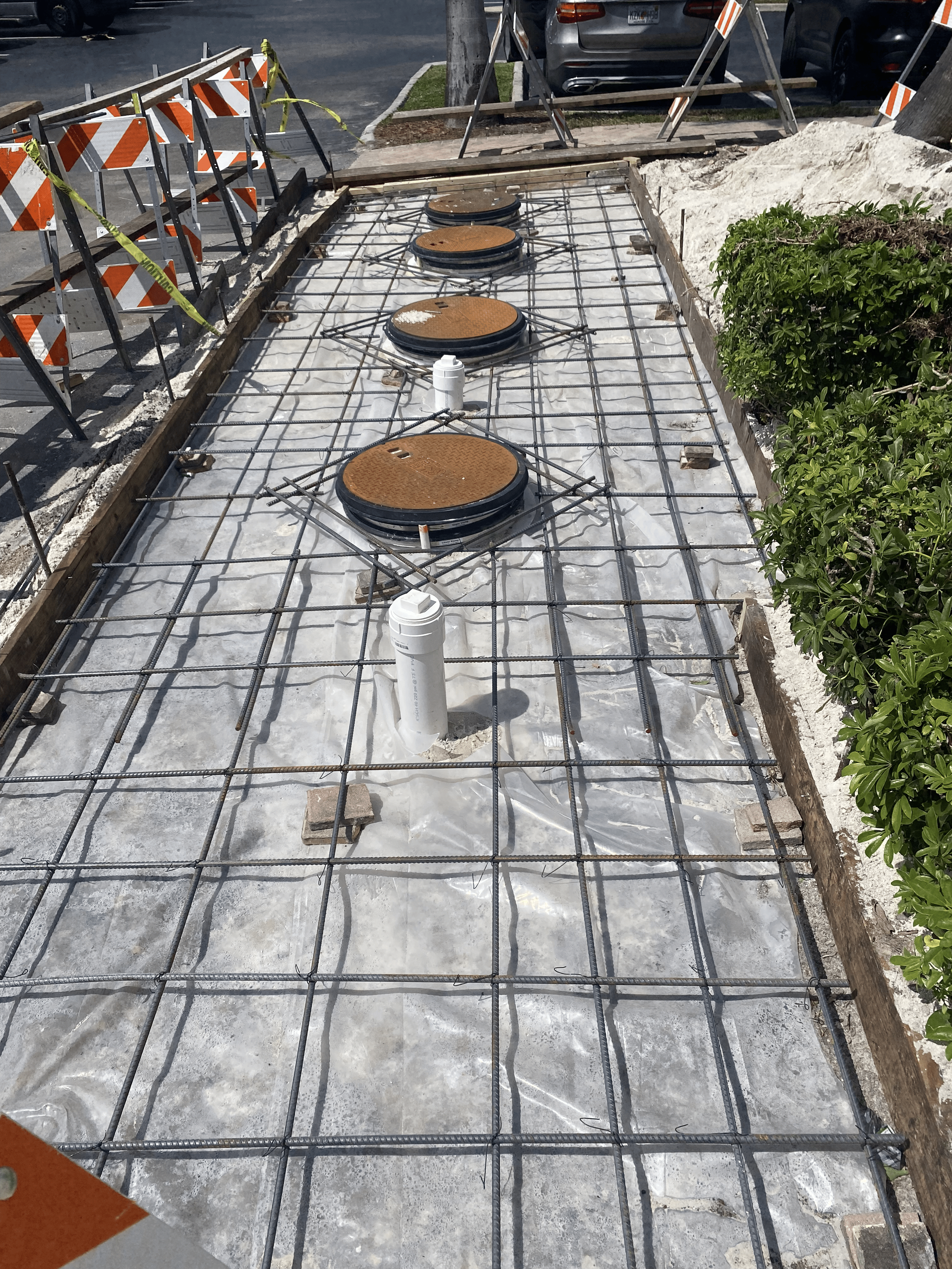 Construction site with metal rebar grid, sewer access points, and barrier.