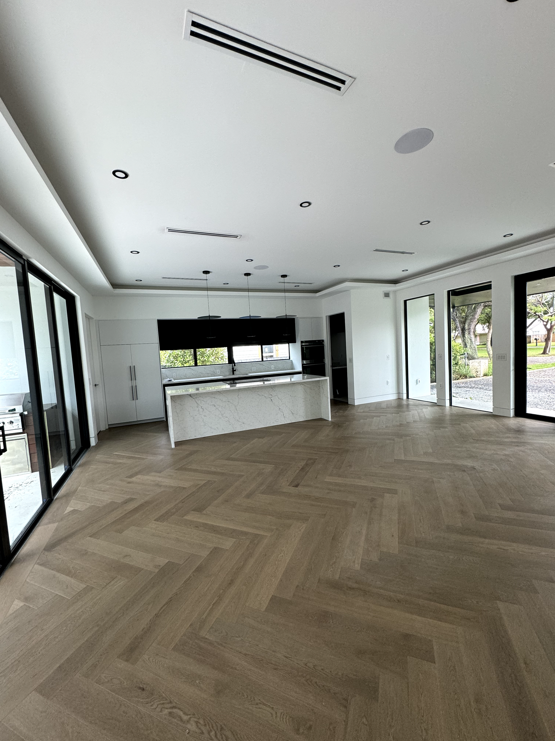 Spacious interior with herringbone wood floors, large windows, and a white kitchen island.
