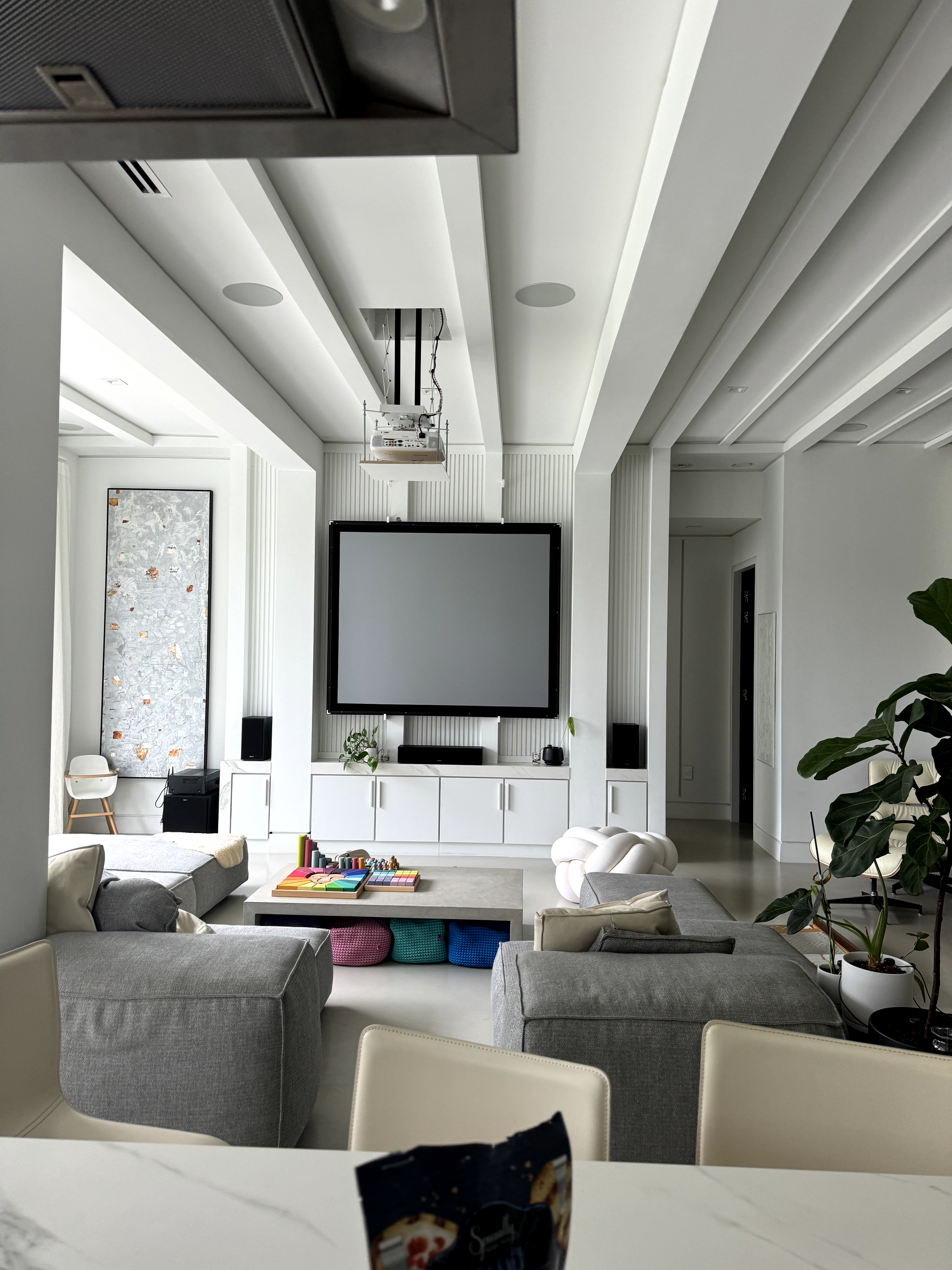 Modern white living room with a projector screen, gray seating, and built-in white cabinets.